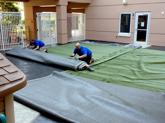 Two men rolling out turf rolls on top of Ultra Base panels