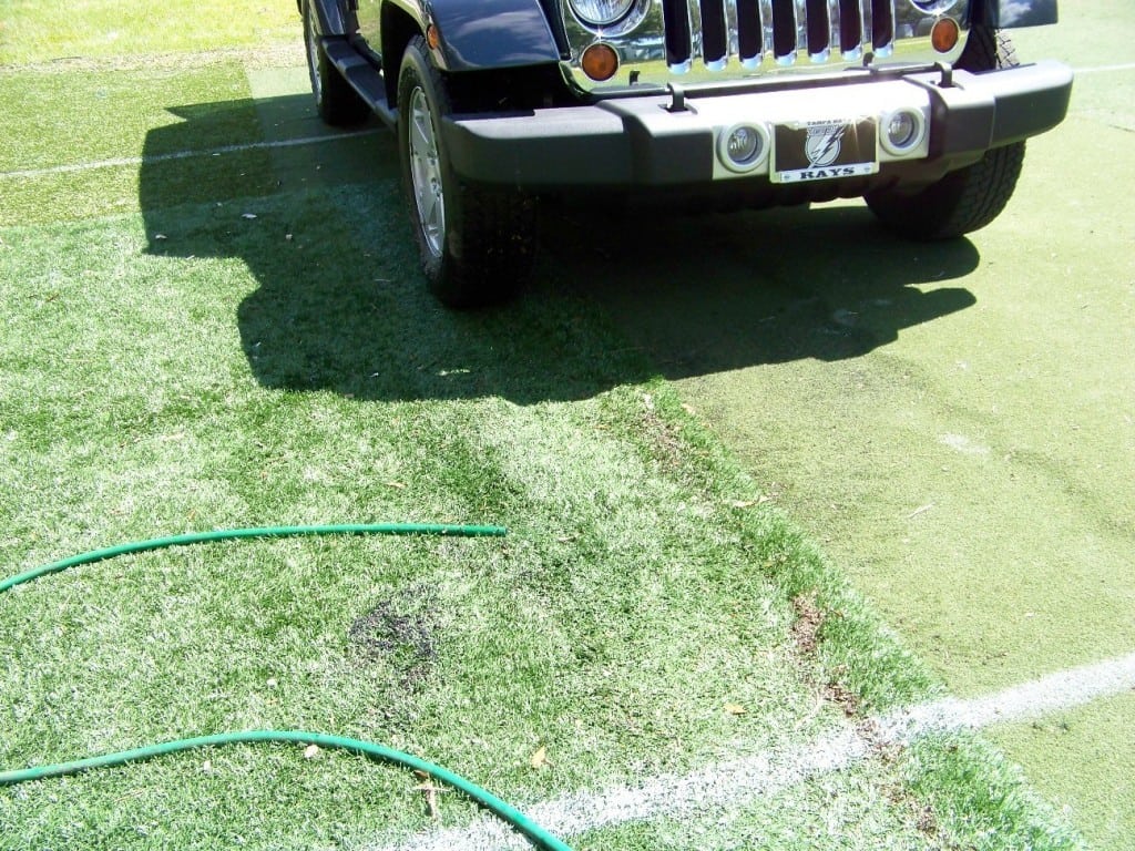 water hose release water on artificial grass as suv drives over turf