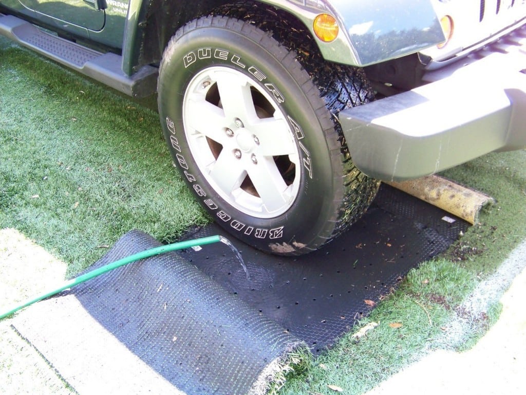 water hose releases water on artificial grass base panel as suv drives over it