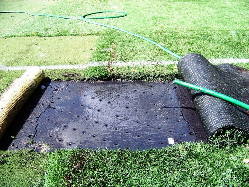 water hose releases water on top of artificial grass base panel