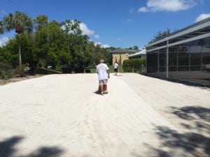 man rakes gravel base for backyard soccer field installation