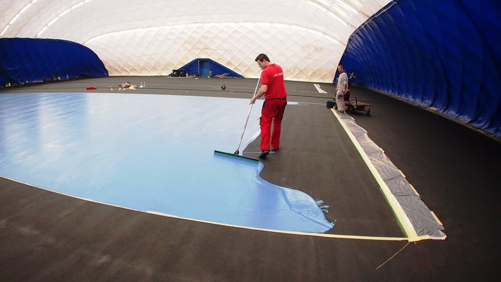 team applies blue paint to tennis court installation