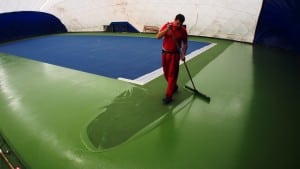 man applies paint to floor of tennis court