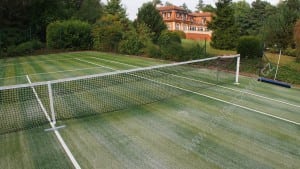 artificial sand filled turf tennis court installation with house in background