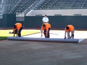 field installers unroll geotextile fabric for football field turf install