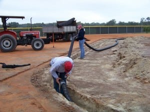 installers placing the tubing for a drainage system during artificial turf installation
