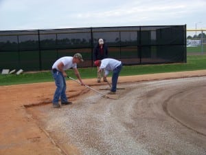 two men raking gravel on dirt field in preparation for artificial turf