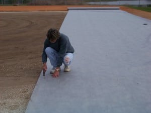 man attaching geo synthetic fabric to dirt floor on field