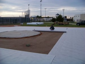 man rolls out geo synthetic fabric over dirt field