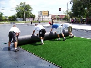 installers help roll out spool of synthetic grass