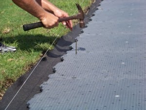 hand using hammer to nail in a base panel for tee line turf