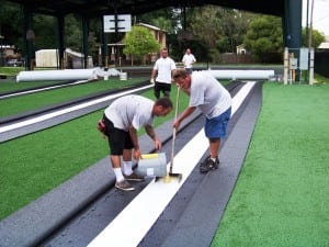 two men seaming artificial grass pieces together on top of panels