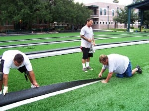men seaming multiple rows of artificial grass