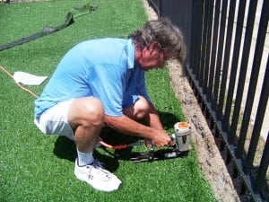 man nailing artificial turf to grown near fence