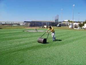 man rolling presser to smooth out artificial turf
