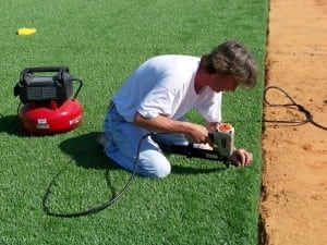 man nailing turf into ground, securing synthetic turf