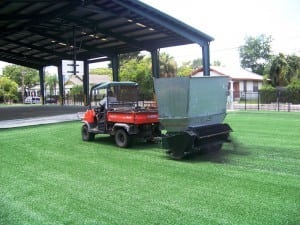 tractor pulling a rubber infill turfco applicator on artificial grass