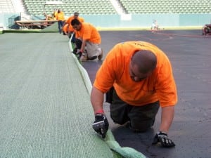 a close up view of field installers cutting artificial turf on base panels during football field installation