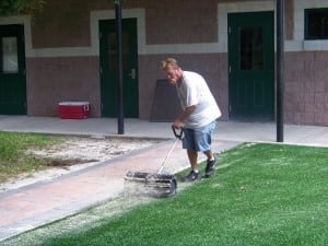 man distributing sand on newly installed artificial grass