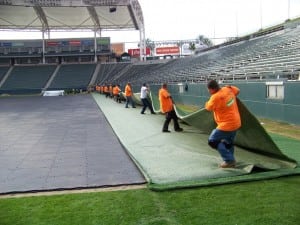 group of field installers unfold a piece of artificial football field turf