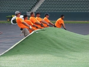 group of field installers spread out artificial football field turf on base panels