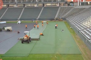 tractor rolling out long pieces of artificial turf on football field