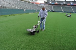 man pressing artificial turf seam on football field