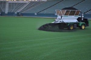 tractor applying infill to artificial football field turf