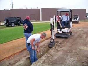 artificial turf field installers dig a trench for base panel system drainage