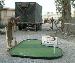 soldier sweeping pre-packaged putting green in iraq