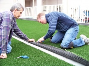 two men cutting pieces of artificial turf