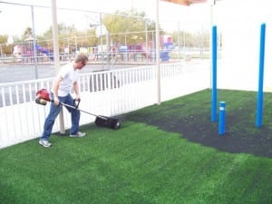 man distributing artificial turf infill on playground installation