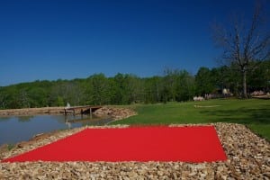 red artificial golf turf next to lake on snag golf course