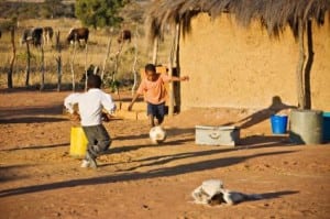 two children in Africa playing soccer on dirt field