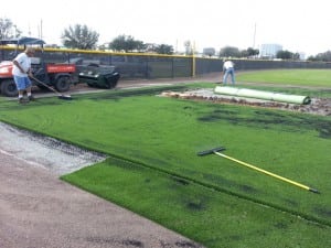 team spreading rubber fill onto artificial turf for baseball field installation