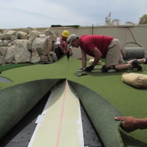 team of installers seam two pieces of artificial turf together in rooftop putting green installation