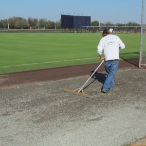 installer raking gravel for Tampa Spring training complex baseball field turf installation