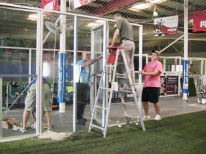 group of men installing plexiglass around indoor artificial turf field