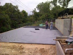 two men lay and connect base panels on top of geotextile for backyard basketball court flooring