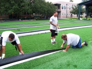 three men seam together pieces of artificial turf