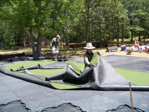 two men laying out artificial grass for outdoor putting green installation