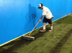 man sweeping in fill onto indoor artificial turf soccer field