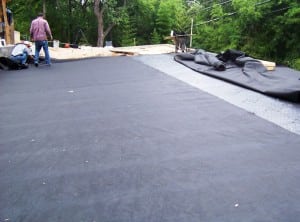 two men rolling out fabric on top of base panels for backyard basketball court installation