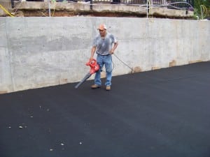 man blowing debris off of fabric in backyard basketball court installation