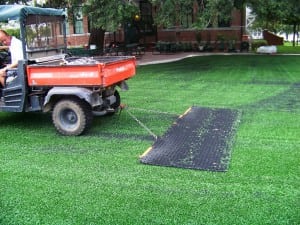 man in tractor sweeps excess artificial turf and infill from soccer field installation