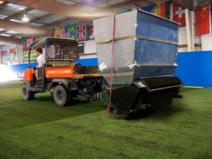 tractor applying rubber infill onto indoor artificial turf soccer field