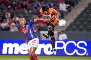 soccer player in the air going after ball as his opponent blocks him