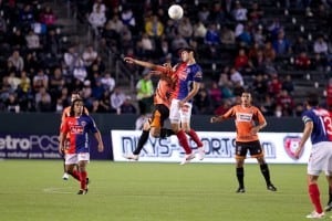 two soccer players jump in the air to head but the ball