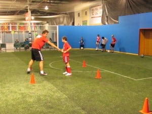 coach training kid on indoor artificial turf soccer field