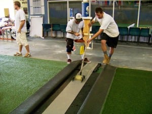 two men spread turf adhesive between two artificial turf pieces